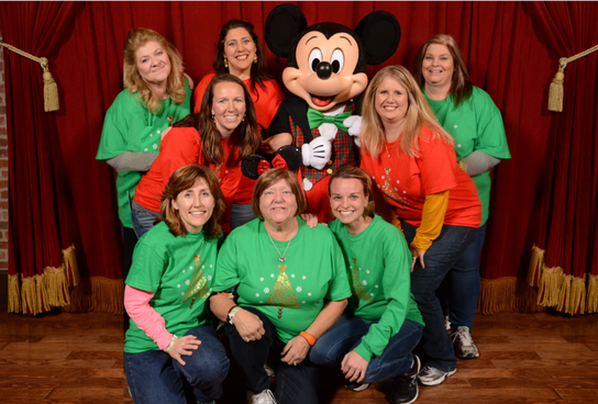 A group of girls wearing green and red T-shirts posing with a Mickey Mouse doll